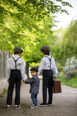 Fototapeta premium Sweet children in vintage clothing, holding suitcase, running in the park