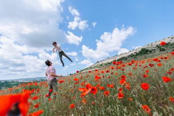 Father throws his son over the red poppy field. The boy laughs, dad happy.
