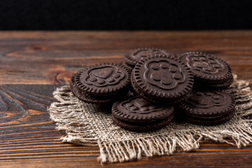 Chocolate cookies with milk filling on dark wooden background.
