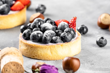 Blueberry and strawberry shortcake. There are hazelnuts, roses and wine corks on the table. Stone background.