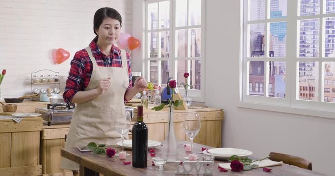 pretty woman setting up putting vase red rose flower on beautiful romantic dinner table. young happy girl prepare ready for valentine day using cellphone taking photo sending to boyfriend online app.