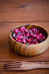 fresh vegetable vegetarian salad in wooden bowl with wooden fork on wooden table, Russian salad vinaigrette, closeup 45 view