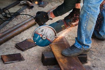 A gloved worker cuts a metal sheet with an angle grinder. Sparks fly from the grinding wheel....