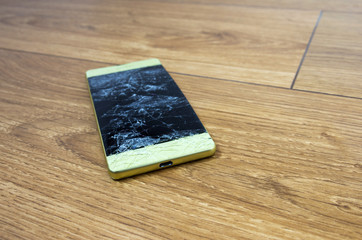 Smart phone with broken screen on the wooden floor. Close-up, selective focus.
