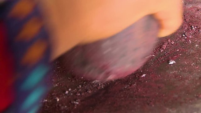 Extreme close-up high-angle still shot of a country side woman grinding collected cochineal insects using stones to make a red dye for wool, Sacred Valley, Andes, Peru