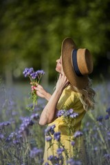 Young beautiful woman blonde in a hat walks through a field of purple flowers. Summer.