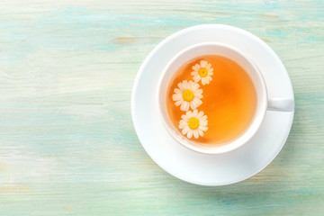 A cup of chamomile tea with steeping flowers, shot from the top on a teal blue background with a place for text