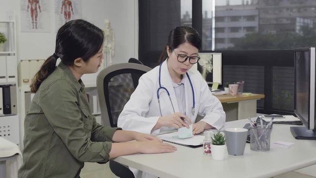 slow motion of young asian female doctor working in office hospital. girl medical staff worker writing on memo giving prescription to woman patient and explaing about medicine. profession health care