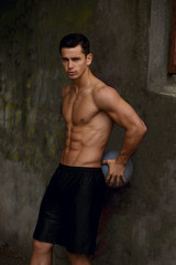 Obraz premium Sexy shirtless muscular young man standing near old urban wall on basketball court. Urban street background.