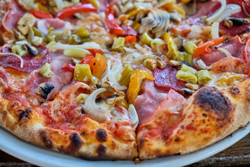 Baked tasty pizza with mushrooms, ham, paprika, salami, onions, mozzarella, pepperoni on a white porcelain plate on a wooden table