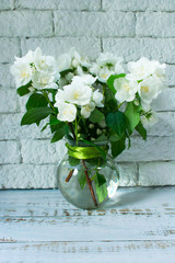 Bouquet of jasmine in a transparent round vase on a white brick wall background.