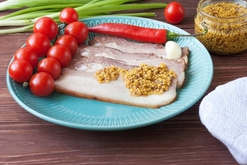 Baked pork belly or bacon sliced into thin slices on a plate with tomatoes, poured with mustard.
