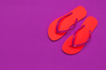Coral flip flops on purple background. Flat lay, top view, copy space. Creative Summer Vacation travel Background. Women's summer footwear. Bright flip flops, trend colors