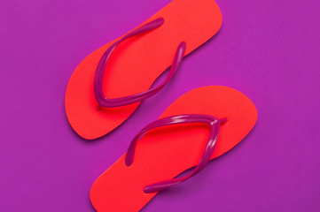 Coral flip flops on purple background. Flat lay, top view, copy space. Creative Summer Vacation travel Background. Women's summer footwear. Bright flip flops, trend colors