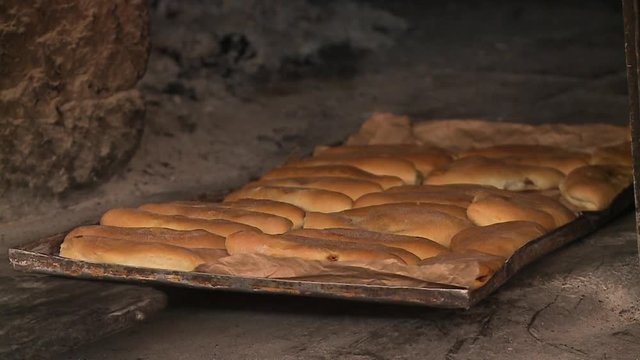 Close-up, high-angle still shot of bread on large flat metallic tray being baked inside a traditional earth oven, Andes Peru