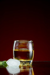 Glass with alcohol in a transparent glass with ice and mint on a red background