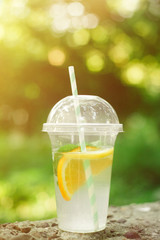 Summer Drink Lemonade with orange and mint in the plastic cup against vivid green background