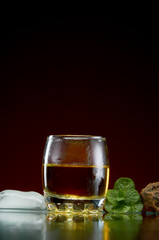 Glass with alcohol in a transparent glass with ice and mint on a red background