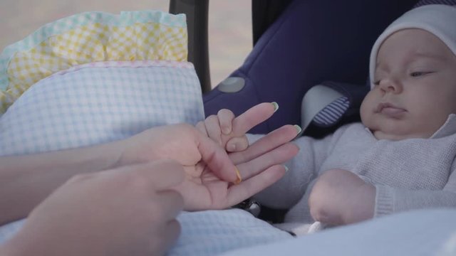 Young happy mother playing and taking care of her newborn cute baby in carriage on a nice spring day