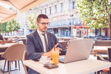 Young man sitting at  street cafe having a conversation on a laptop wearing a headphones