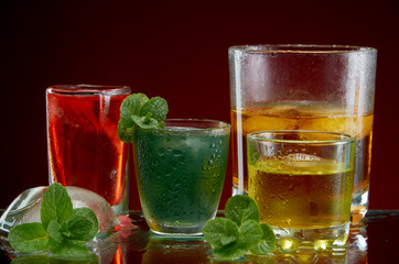 Three different alcoholic drinks in clear glasses with ice and mint on red background