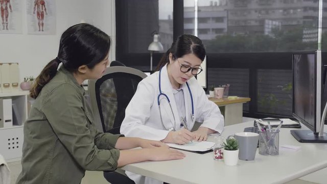 female doctor writing on memo at desk making prescribing medication in clinic office. professional woman medical staff worker explaining report situation to lady giving prescription in hospital.