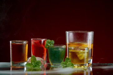 Alcoholic drink with ice and mint in a light smoke on the red background