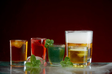 Different alcoholic cocktails with ice and mint with light smoke on a red background