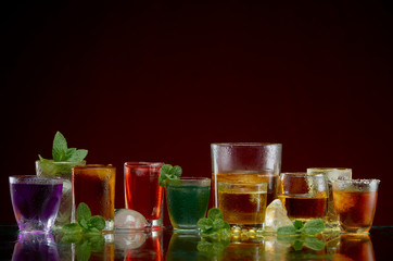 Fototapeta na wymiar Different alcoholic drinks in clear glasses with ice and mint on red background