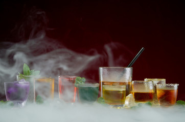 Various alcoholic cocktails with ice and mint framed by smoke on a red background