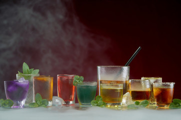 Various alcoholic cocktails with ice and mint framed by smoke on a red background