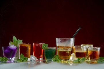 Glasses with various alcoholic drinks with ice and mint on red background