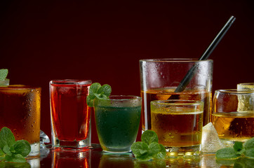 Various alcoholic cocktails in clear glasses with ice and mint on a red background