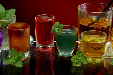 Colored alcoholic drinks with ice and mint on red background