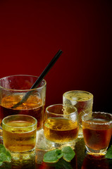 Colored alcoholic drinks with ice and mint on red background