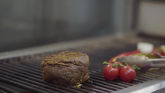 Chef preparing tasty meat on the grill, turning it with tongs close-up. Red charcoals on the bottom. Food preparation in the restaurant kitchen