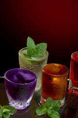 Colored alcoholic drinks with ice and mint on red background