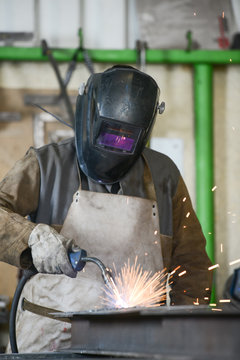handsome man workshop welding iron spark fire hot steel with power GMAW welder and protective gear