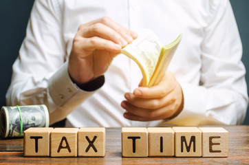 Wooden blocks with the word Tax time and taxpayer with a money. Property / income annual taxes. The...