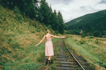 Young girl walking on the railway. Woman in pink dress walking on railroad tracks.