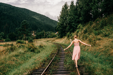 Young girl walking on the railway. Woman in pink dress walking on railroad tracks.