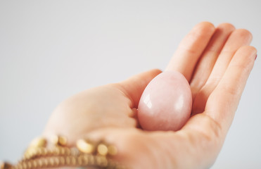 woman holding in hand a vaginal (yoni) egg. Rose quartz crystal jade egg. Copy space