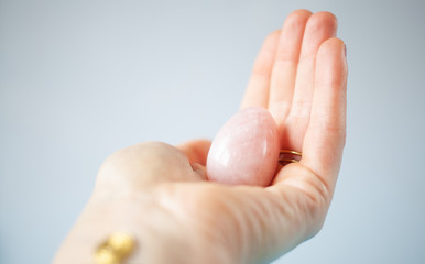 woman holding in hand a vaginal (yoni) egg. Rose quartz crystal jade egg. Copy space