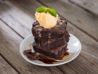 Chocolate brownies stacks and vanila ice cream on top, wooden background