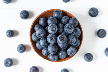 Blueberries in a wooden bowl on white table in top view or flat lay, fresh fruit