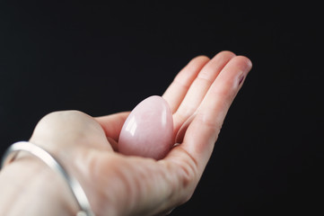 woman holding in hand a vaginal (yoni) egg. Rose quartz crystal jade egg. Copy space