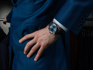 A man in a classic suit with a clock on his hand holds his hand on his belt