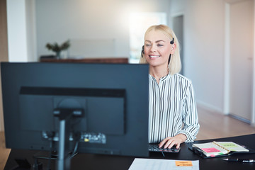 Smiling businesswoman using her computer while talking on a head