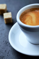 Cup of coffee and two brown sugar cubes on dark stone background. Close up.