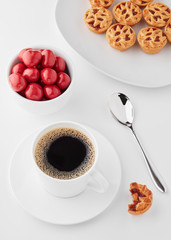 White coffee cup, red sugar coated pills, and apple tarts on a white table